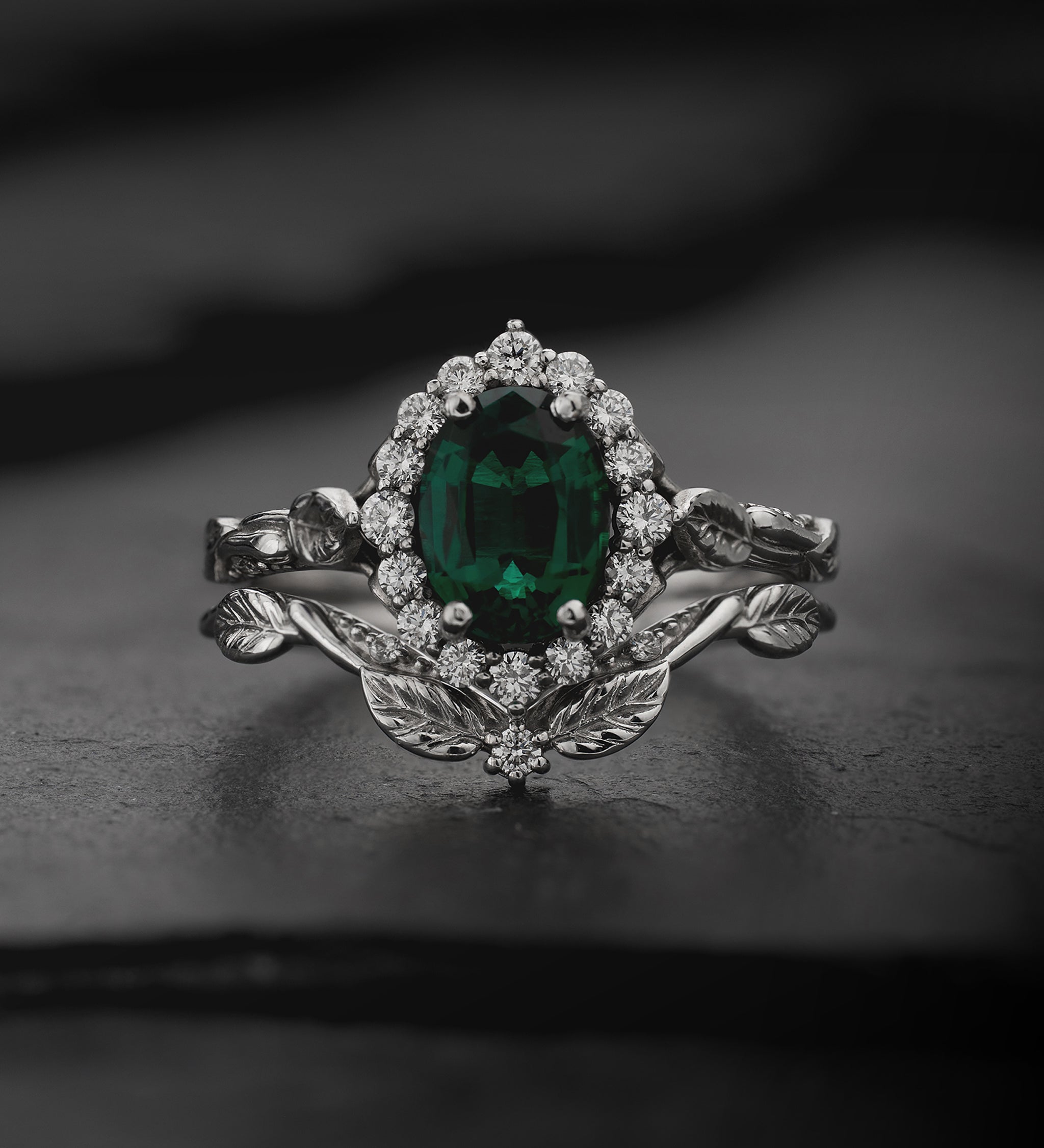 White gold ring with diamond halo and an oval green gemstone on a dark background