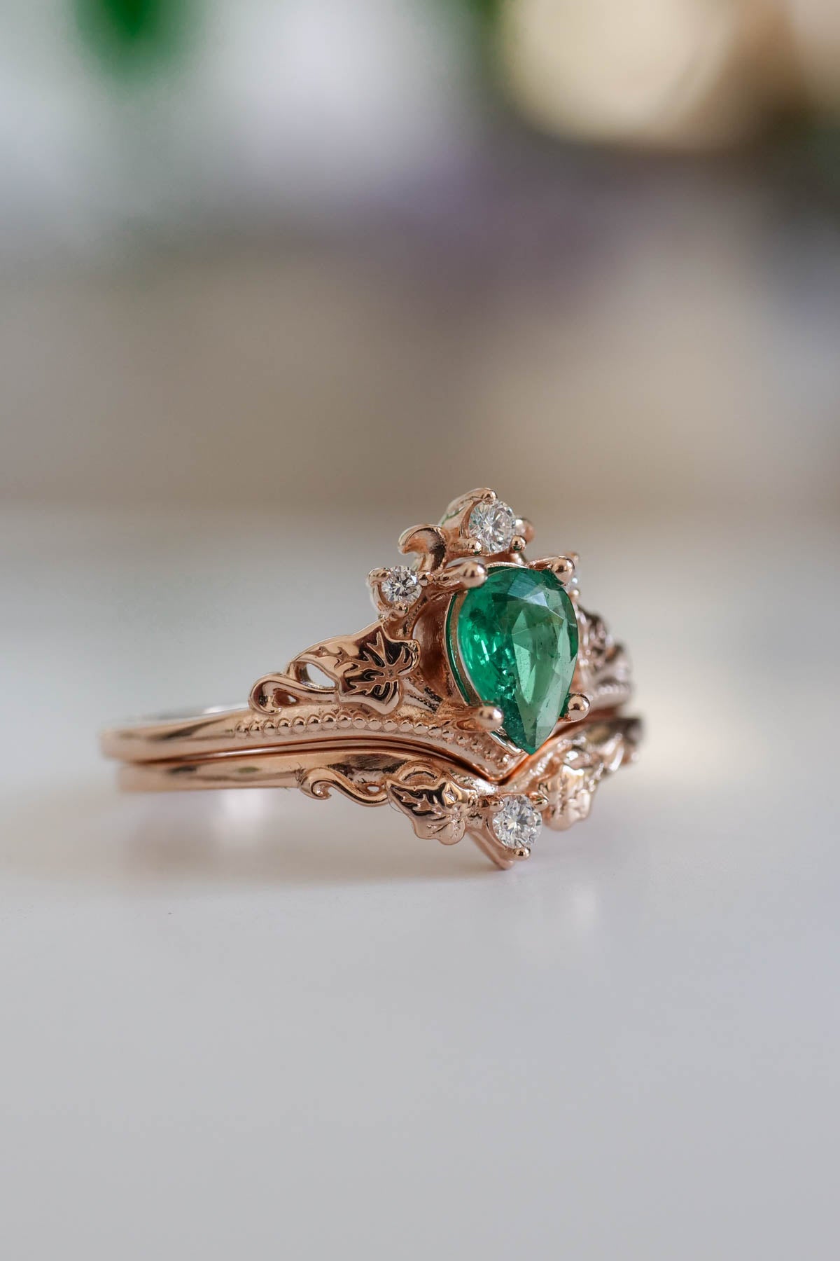rose gold engagement ring with pear cut emerald and small side diamonds stones