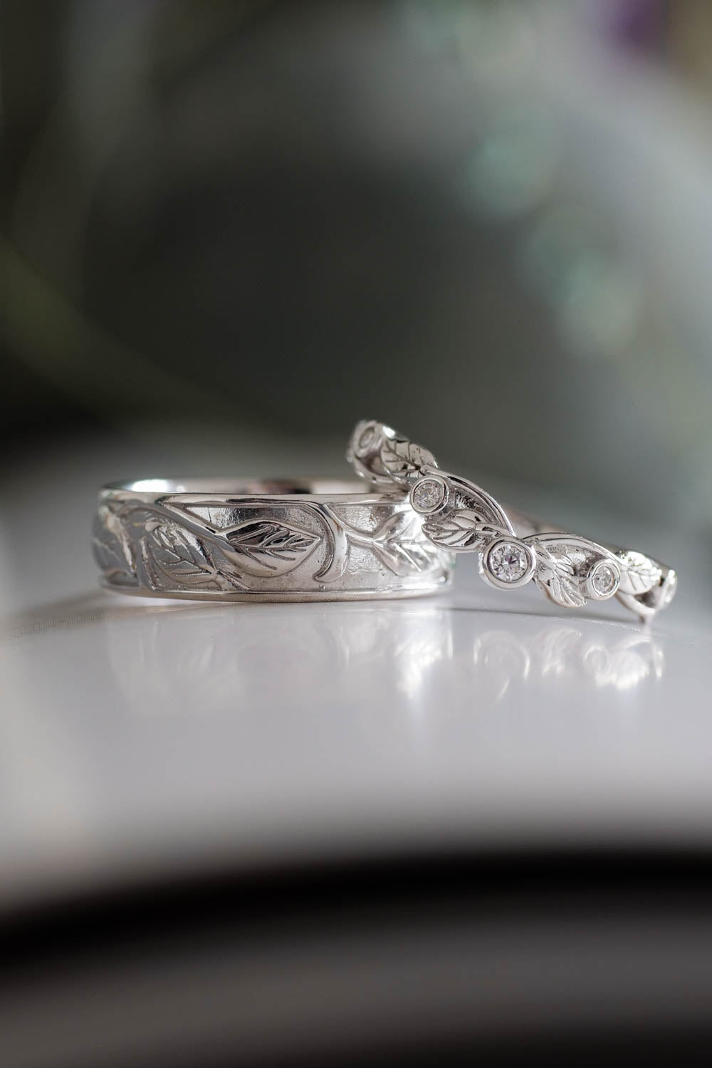 white gold weeding rings for her and him together on the table, leaves details on the gold